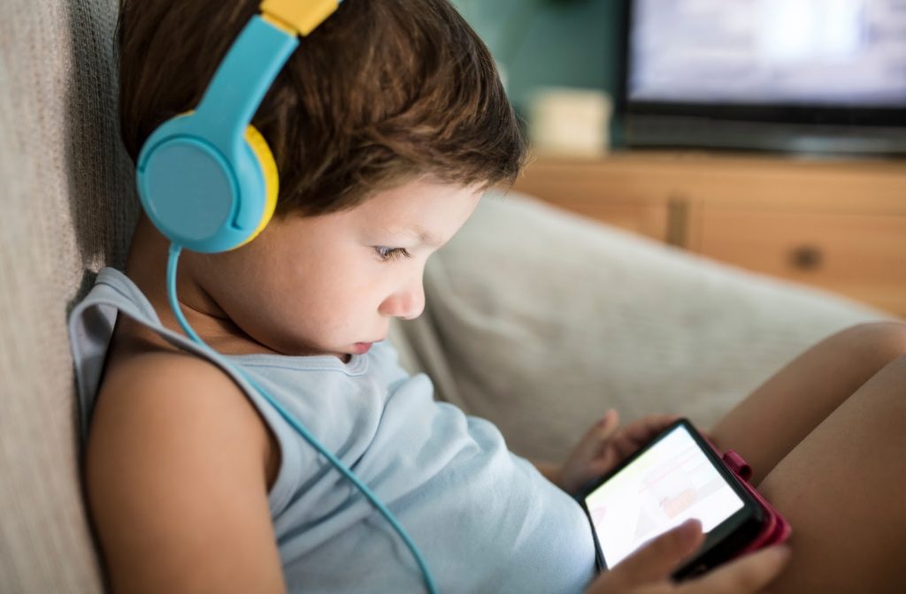 A child sitting with headphones on looking at a screen impacting their eye health