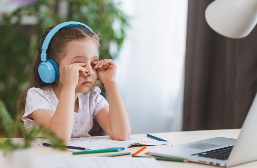 A little girl rubbing her sore, tired eyes from looking at a laptop screen for too long