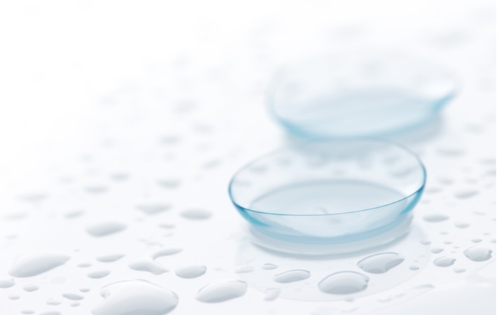 Two contact lenses laying on a white surface with water droplets