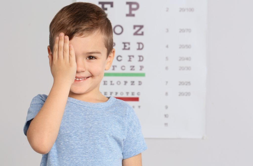 A young boy at the optometrist performing an eye exam and covering his right eye with his right hand
