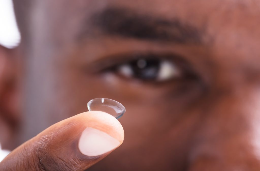 A zoomed-in view of a man's fingertip with a contact lens resting on it