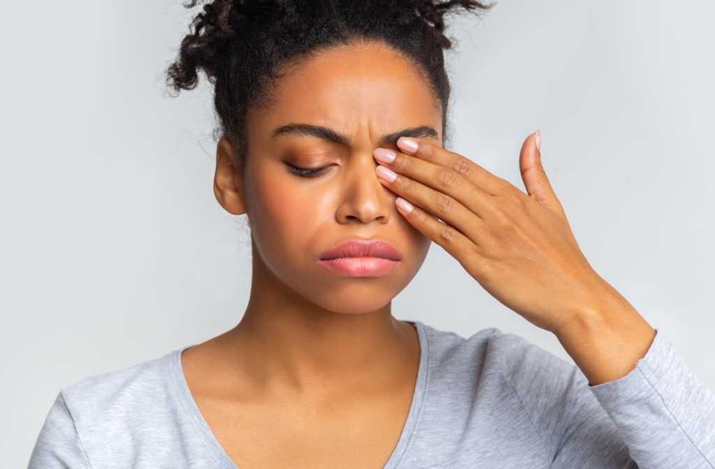 A woman placing her left hand on her left eye as she is getting discomfort when she blinks her eyes