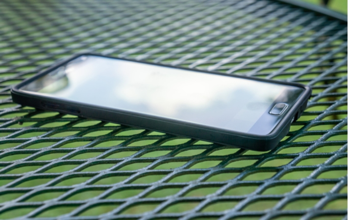 A phone laying face up on a table outside with glare reflecting off the screen, making it difficult to read what's displayed