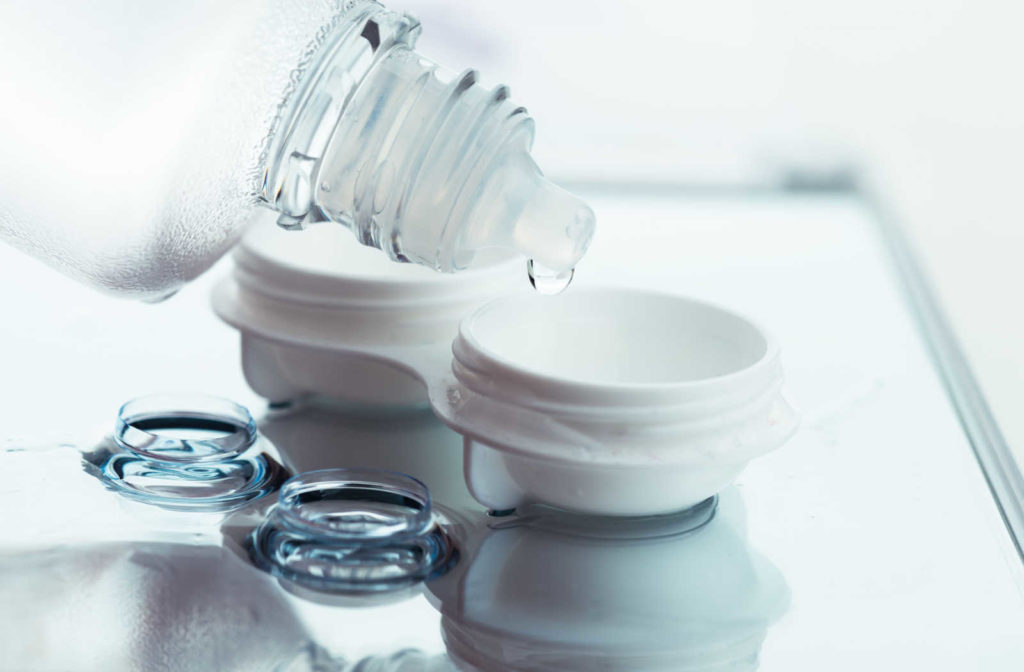Contact lens solution being put into a contact lens case while a pair of contact lenses sit on the surface in front.