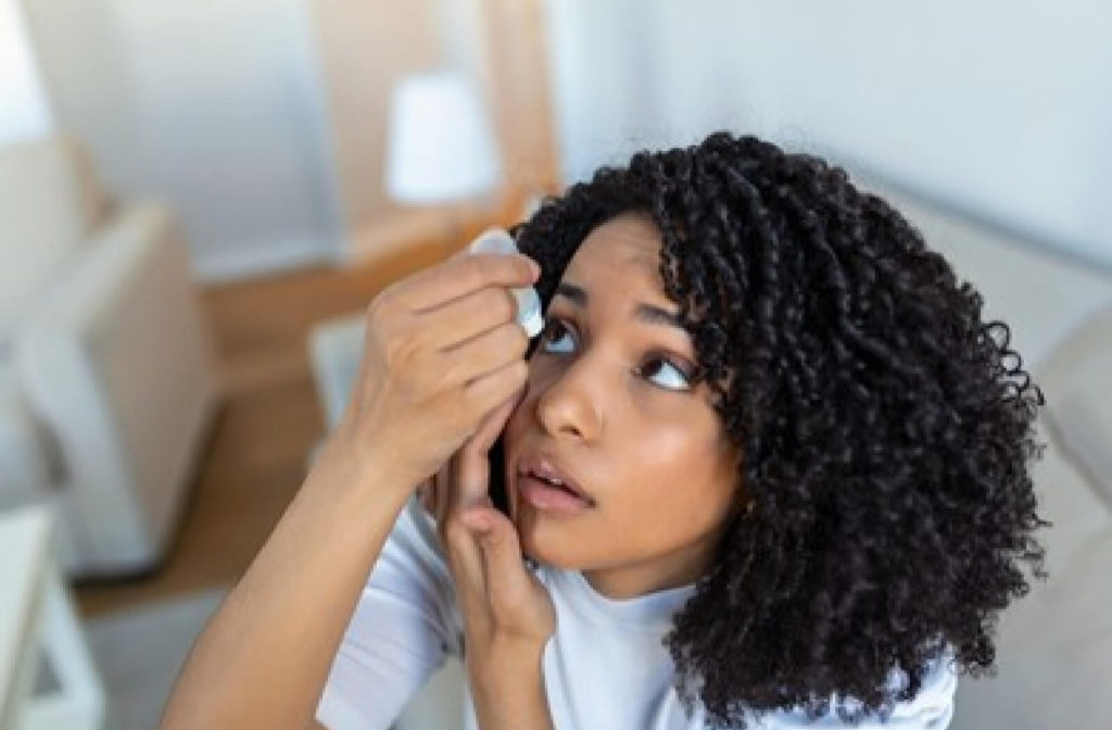 A woman is using contact lens- safe eye drops to add some moisture before putting her contact lenses in.