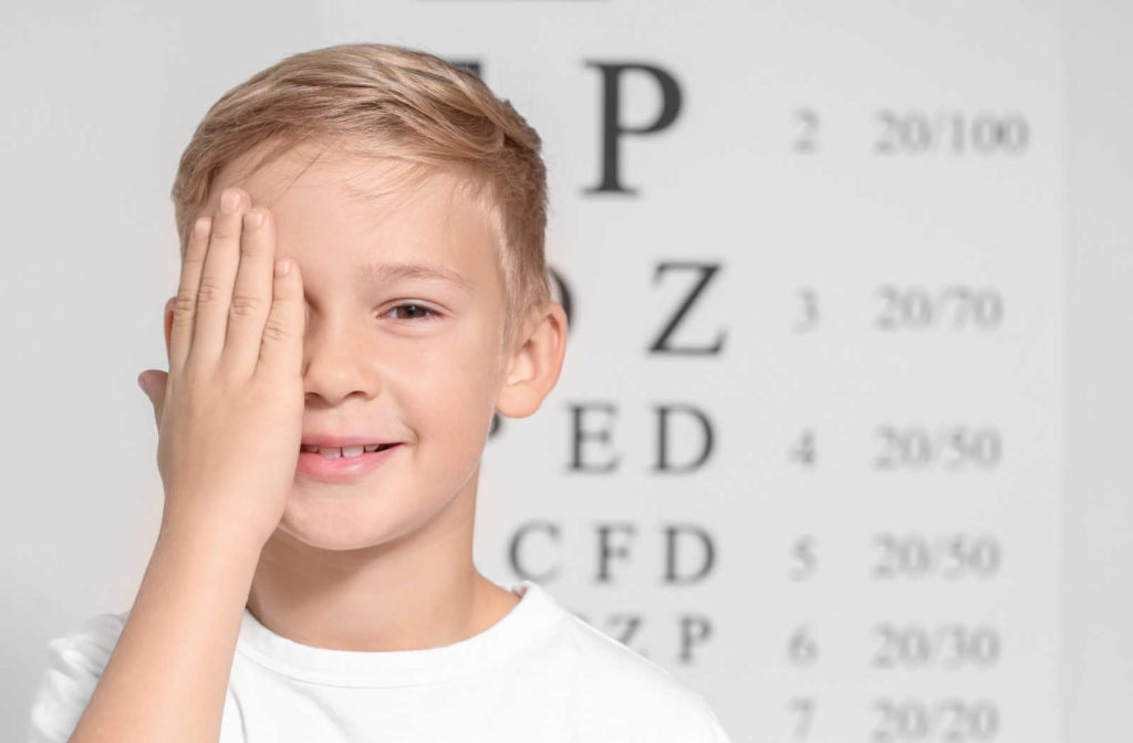A boy in an eye clinic is undergoing a visual acuity test, by covering his eye while looking into a Snellen chart in a distance.