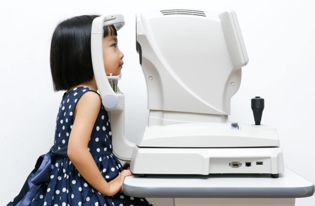 A female child is ungeroing an eye exam with the use of autorefractor to measure how light changes as it comes into the eye, giving an accurate estimate of prescription.