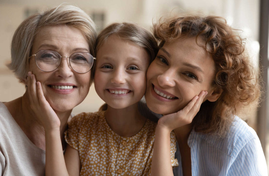 Three generations of woman with their heads together smiling, showing how vision and eye health can be hereditary