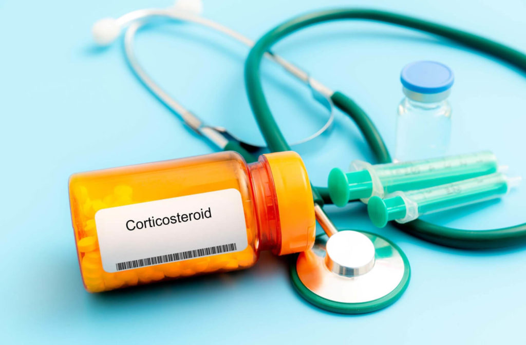 A bottle of corticosteroids, a stethoscope, and a syringe on the background. Steroids cause changes in the aqueous fluid outflow system resulting in increased eye pressure.