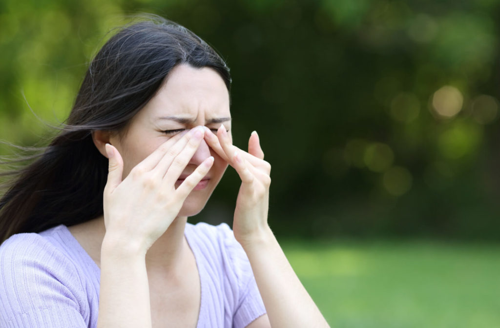 A woman rubbing her itchy eyes outdoors.