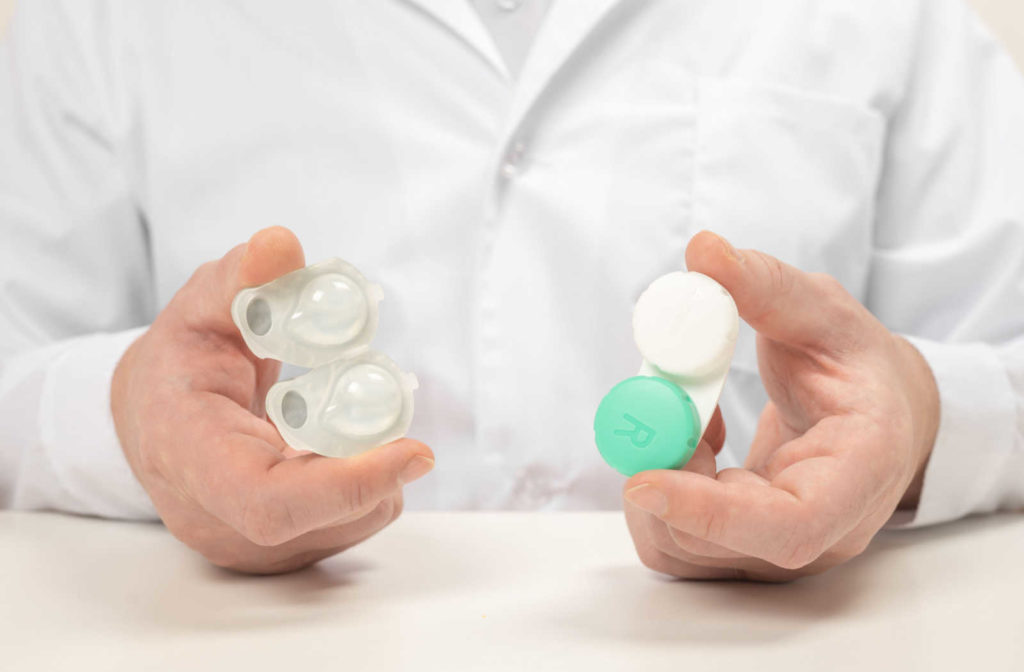 An eye doctor holding a blister pack of contact lenses in one hand and a contact lens case in the other hand.