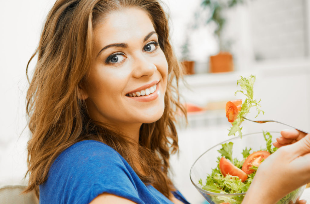 Close-up of a woman in a blue shirt eating a salad and smiling to help maintain her eye health.