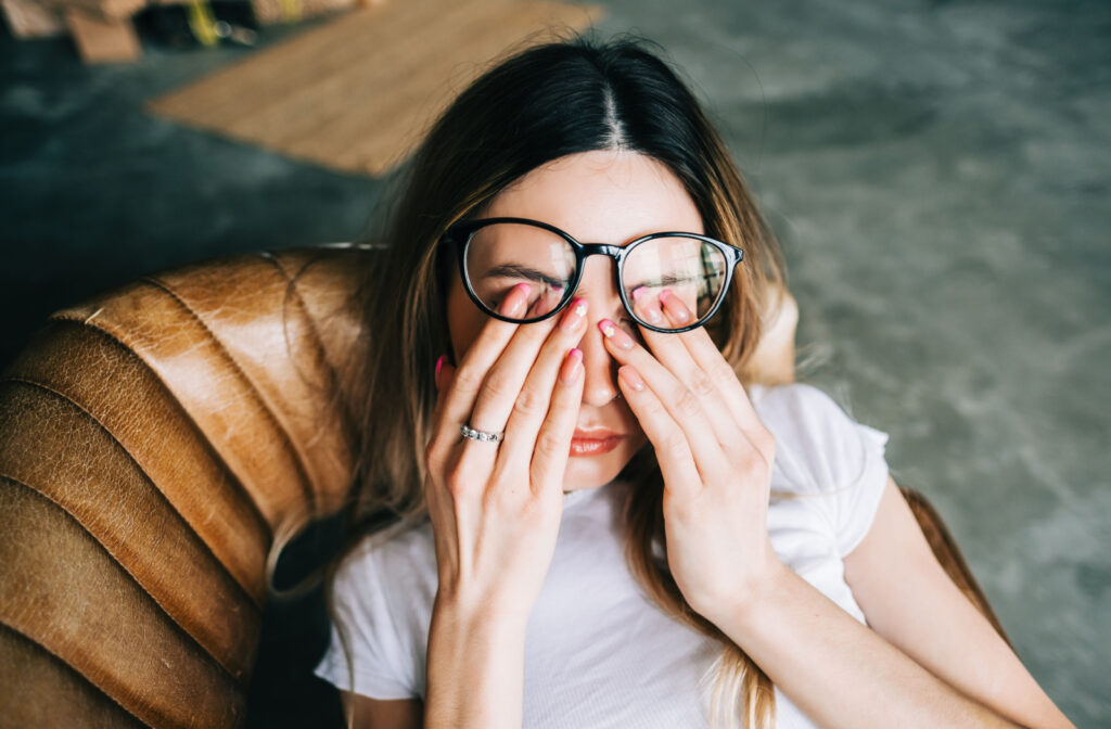 A woman sitting on a couching rubbing her eyes underneath her eyeglasses.