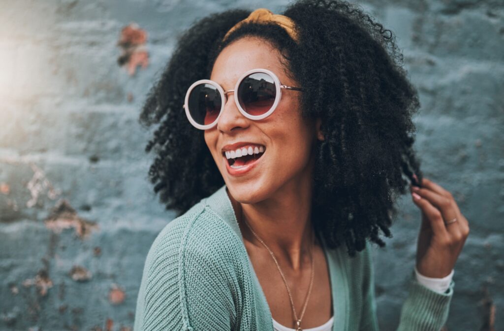 Smiling young woman wearing sunglasses in front of a brick building.