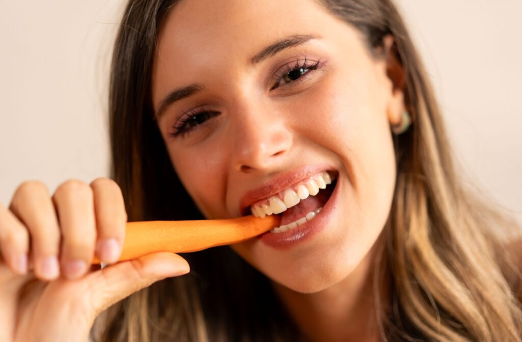 Close-up of a person smiling as they bite into a carrot.