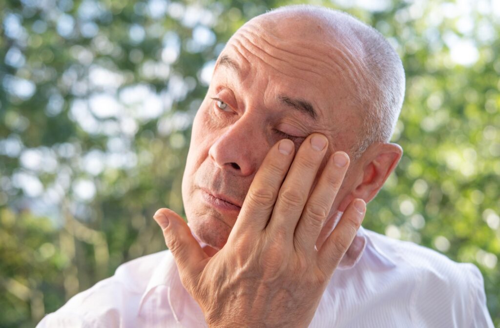 A person outdoors winces and rubs the side of their eye in pain