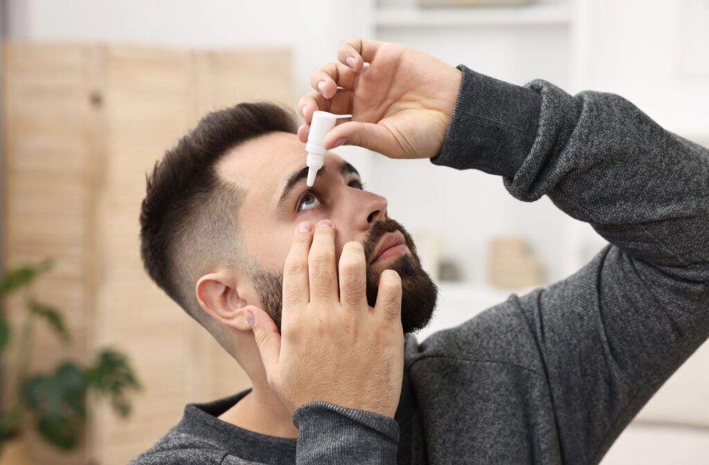 A person holds their eye open to apply eye drops to treat their dry eyes.