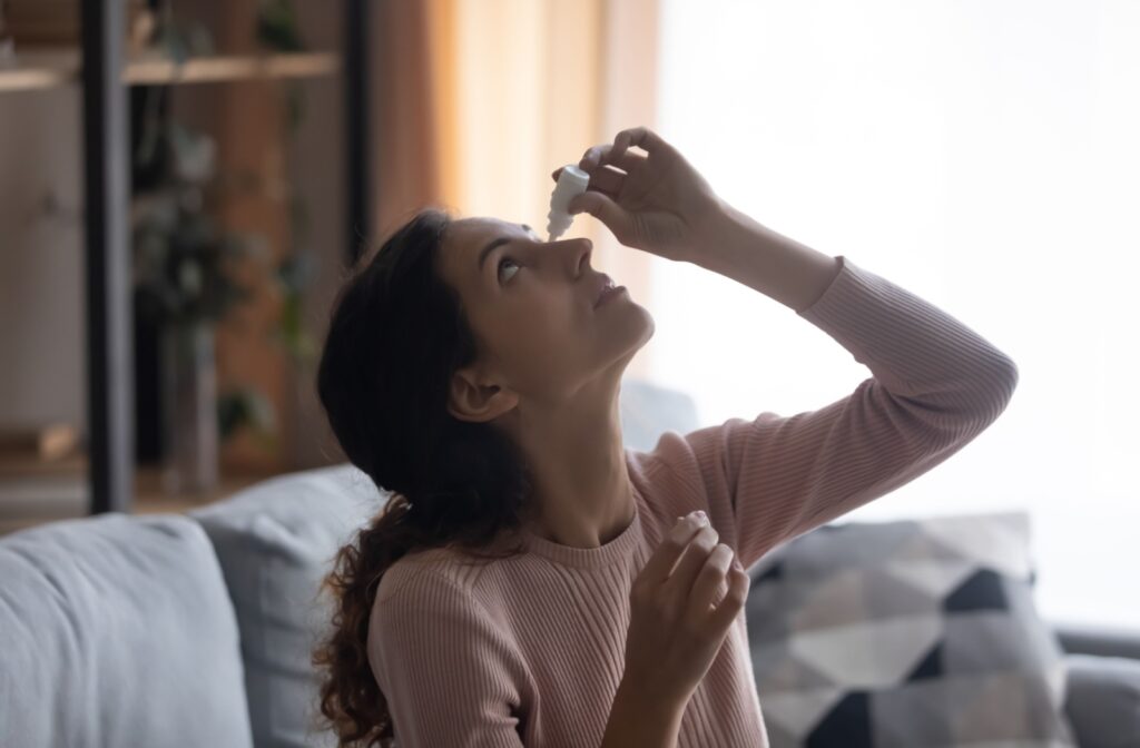 A young adult on their couch using eye drops in the morning to find relief from their dry eyes.