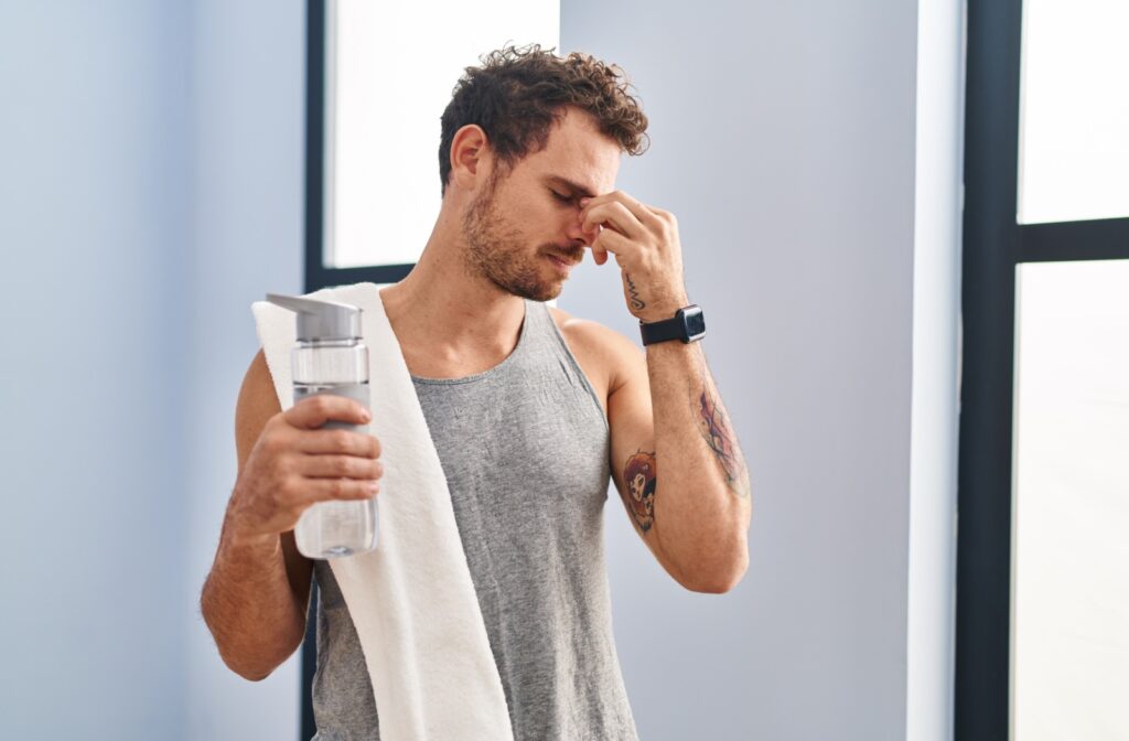 Young man holding a water bottle and rubbing his eyes, suggesting dry eyes due to dehydration.