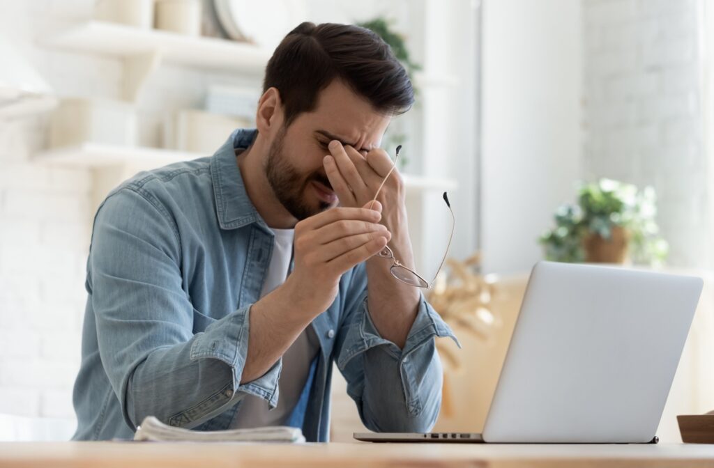 A young man rubs at his eyes due to discomfort from digital eye strain.