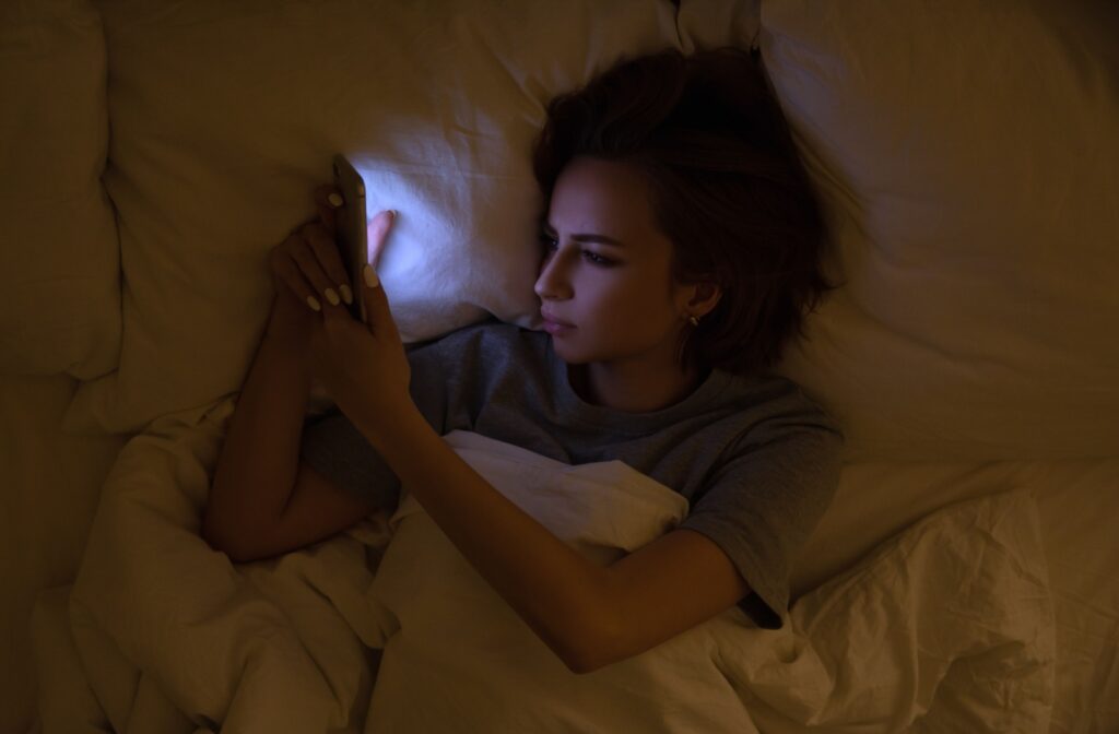 A woman using her phone in the dark in bed. A blue glow is casted across her face.