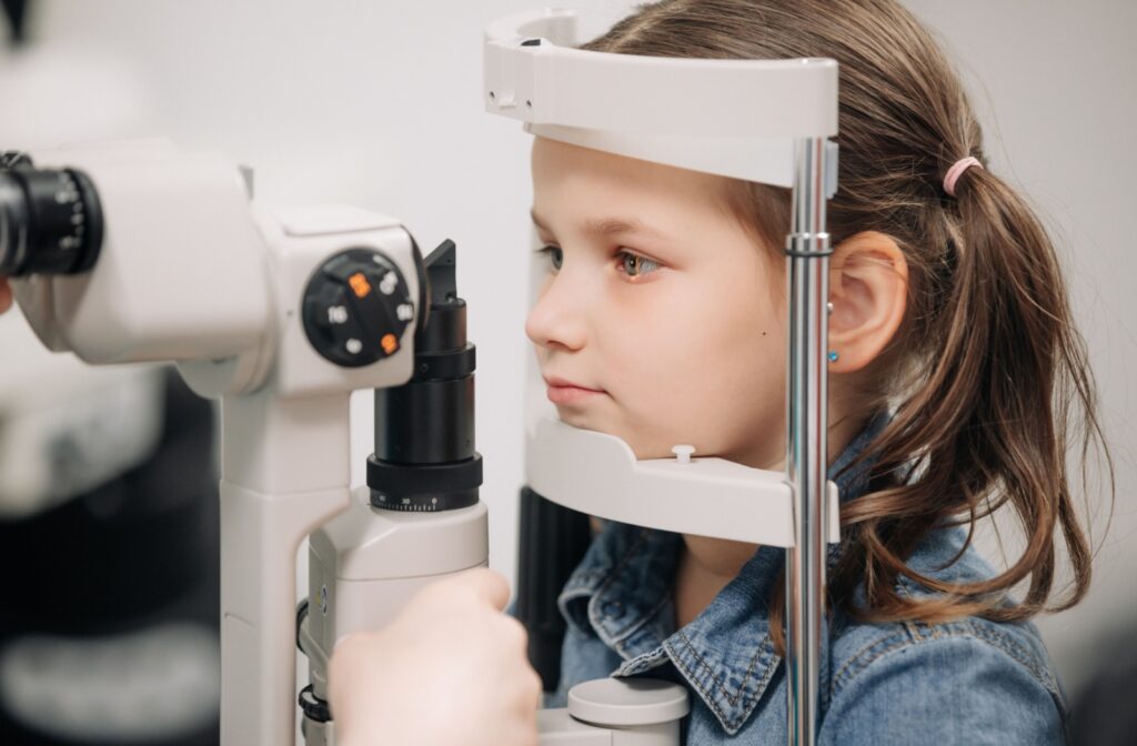 A child sits patiently as their eye doctor examines their eyes with a slit lamp.