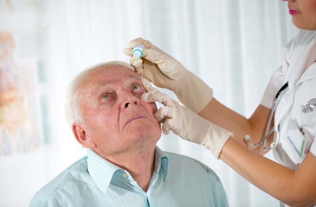 An eye doctor places eye dilating drops in a senior's eyes to perform a dilated eye exam.