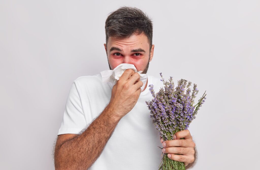 A person holding wild flowers suffering from red irritated eyes due to allergies.