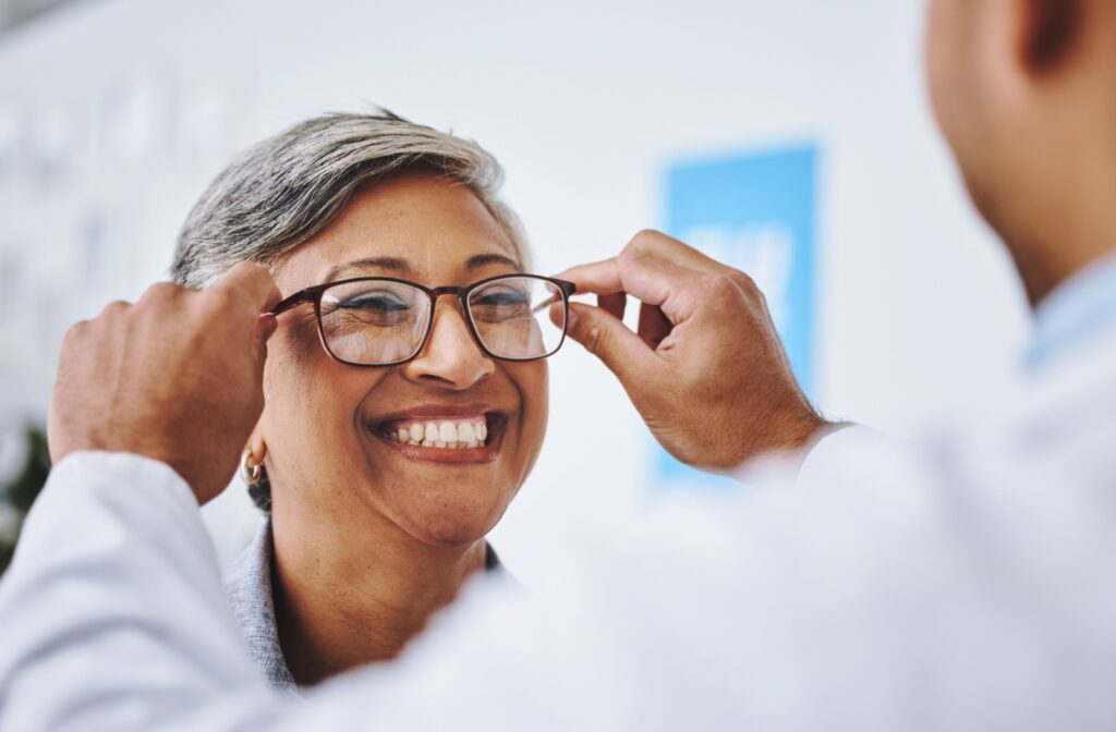 Optometrist helping a smiling patient put on new eyeglasses during an appointment.