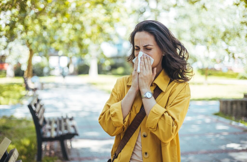 Woman outside blowing her nose into a tissue due to allergies