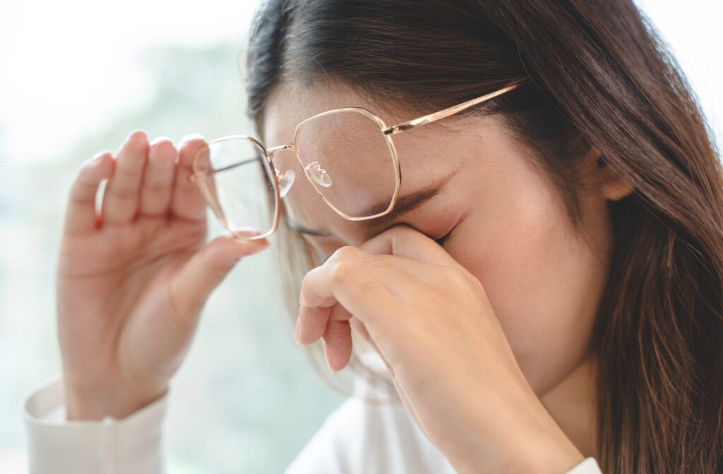 A person holding their glasses over their forehead so they can rub their eyes