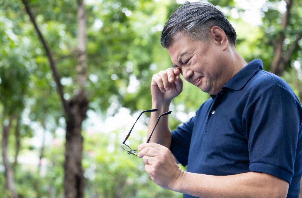 Man holding his glasses in one hand and rubbing his eyes with his other hand while outside