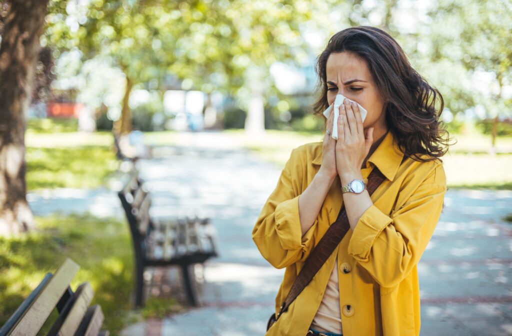 A person outside blowing their nose into a tissue due to seasonal allergies
