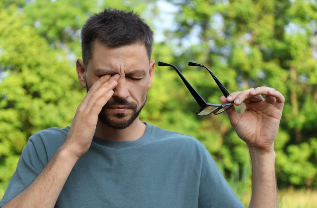 A person outside removing their glasses with one hand and using their other hand to rub their eye
